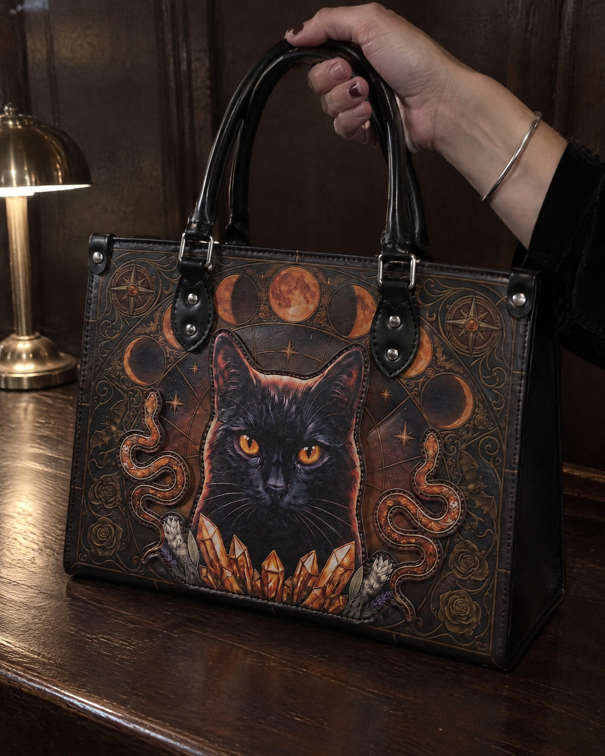 "Hexacat" appliqué leather handbag standing on a dark bar counter, her hand on the handles, a brass lamp beside it